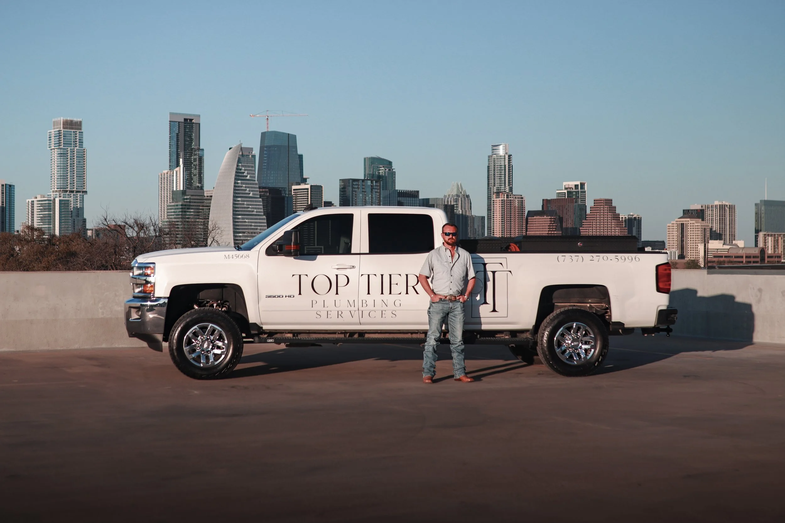 Logan Lasater standing in front of the Top Tier Plumbing Services branded truck with Austin skyline